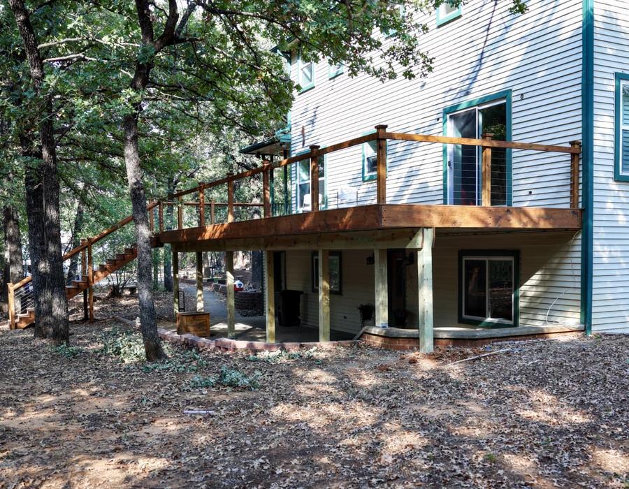 Elevated wood deck with stairs and cable railing attached to a two story home